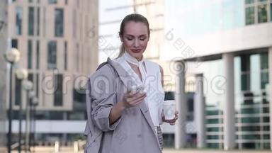一位年轻的女商人站在市中心，用智能手机端着一杯咖啡